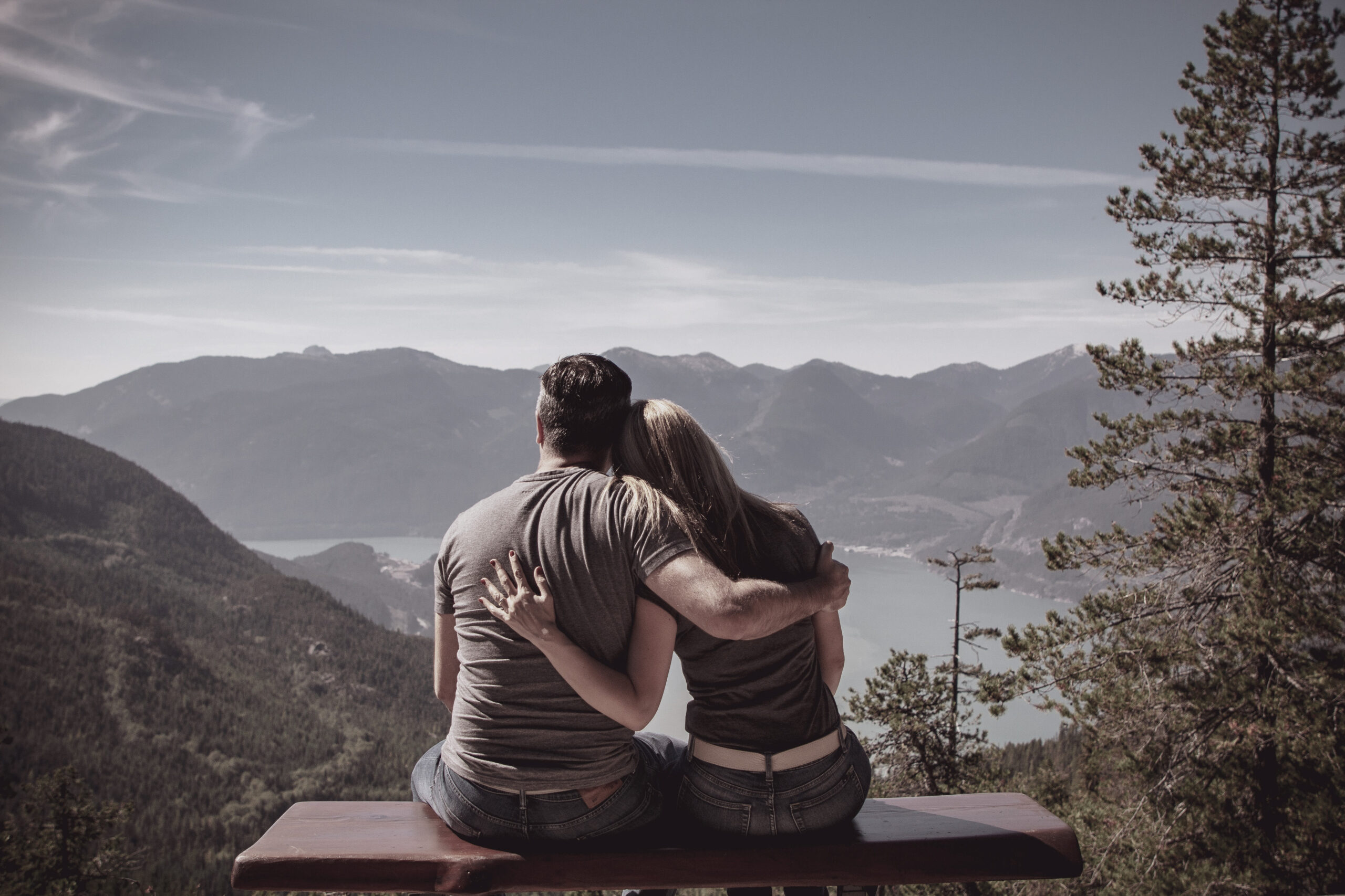Couple sitting on a bench embracing while looking out at scenic mountain and lake views, symbolizing connection and luxury travel experiences